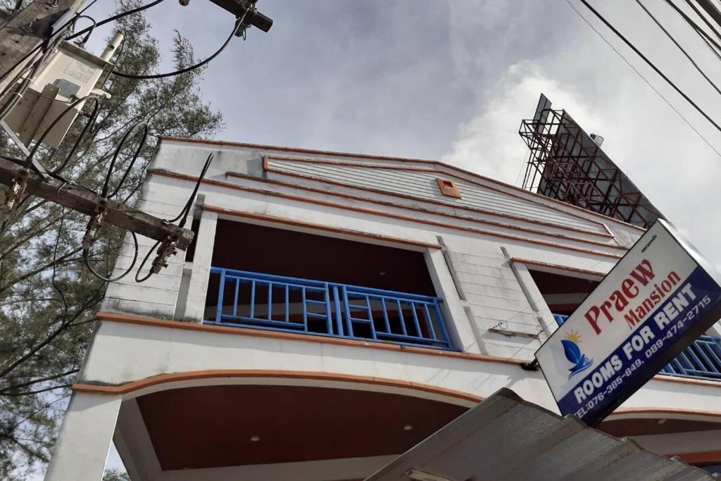 a white building with blue windows and a sign at Praew Mansion in Kamala Beach