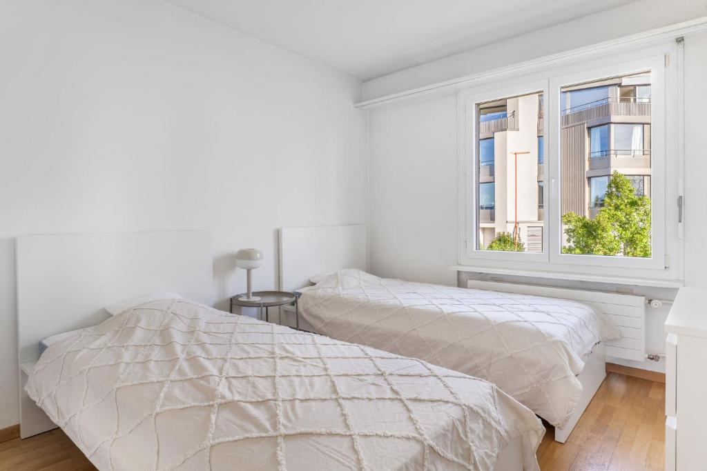 two beds in a white room with a window at EXQUIS Design 3-Room Apartment KNOLL I Zurich Lake View I Balcony I Family-Friendly in Männedorf