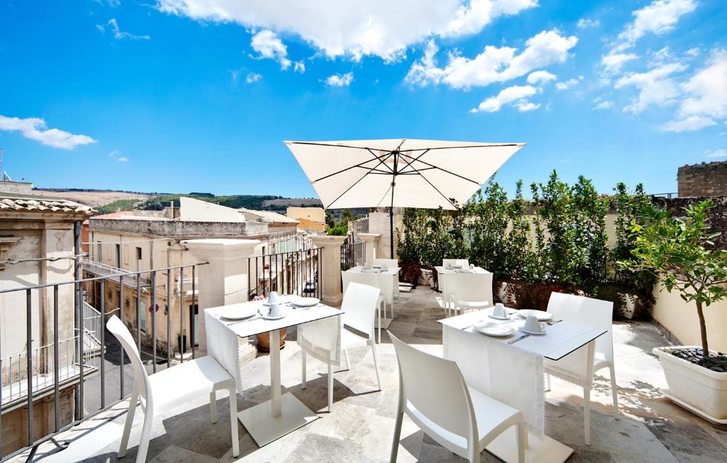 un patio con tavoli e sedie bianchi e ombrellone di Epoca - Camere con stile a Ragusa