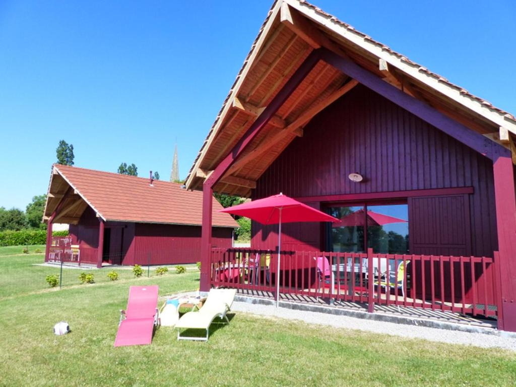 a red barn with chairs and umbrellas in the grass at Gîtes Cosy au Bocage Bourbonnais avec Confort Inclus - FR-1-489-235 in Meillard