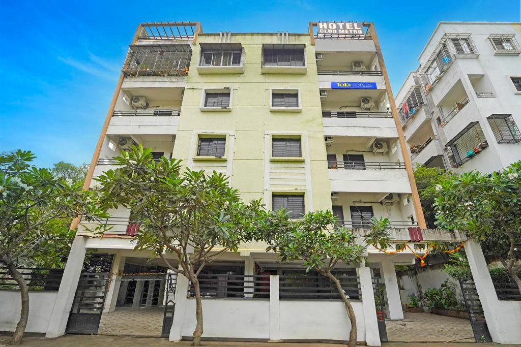 a tall yellow building with trees in front of it at FabHotel Club Metro in Nagpur