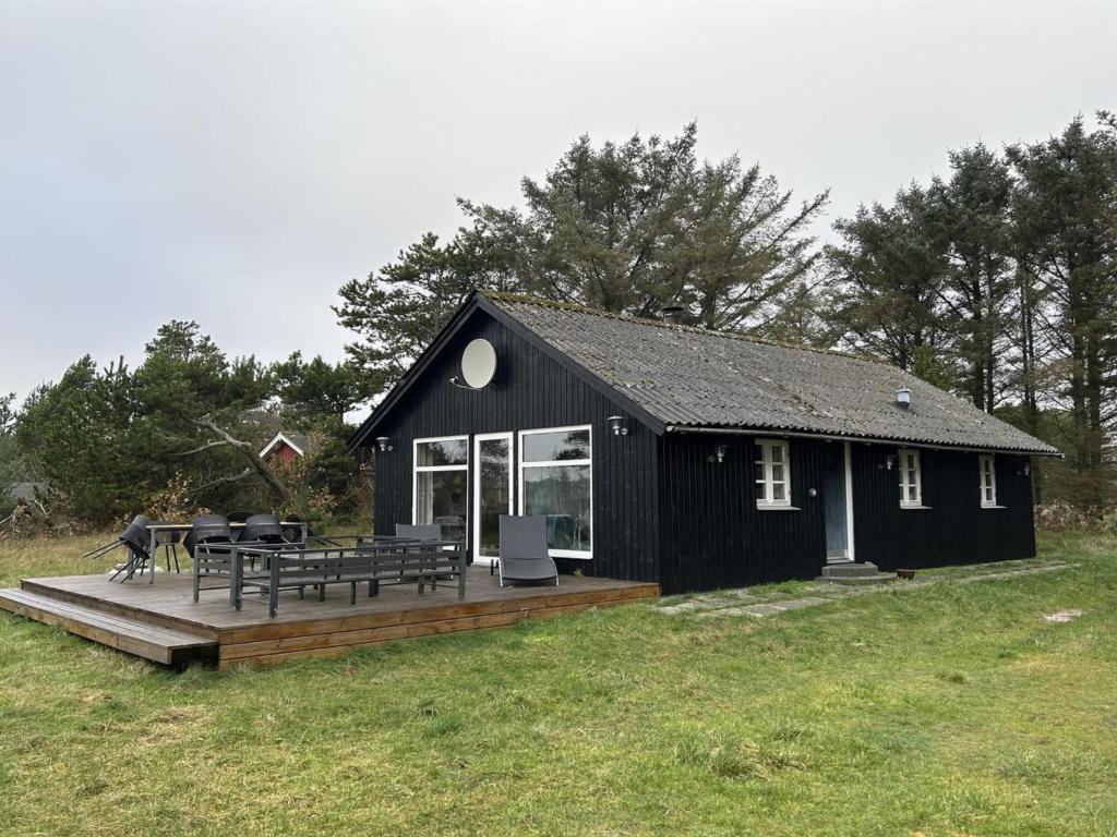 Una cabaña negra con terraza y mesas de picnic. en Holiday Home Brawith - 700m to the fjord by Interhome, en Ringkøbing