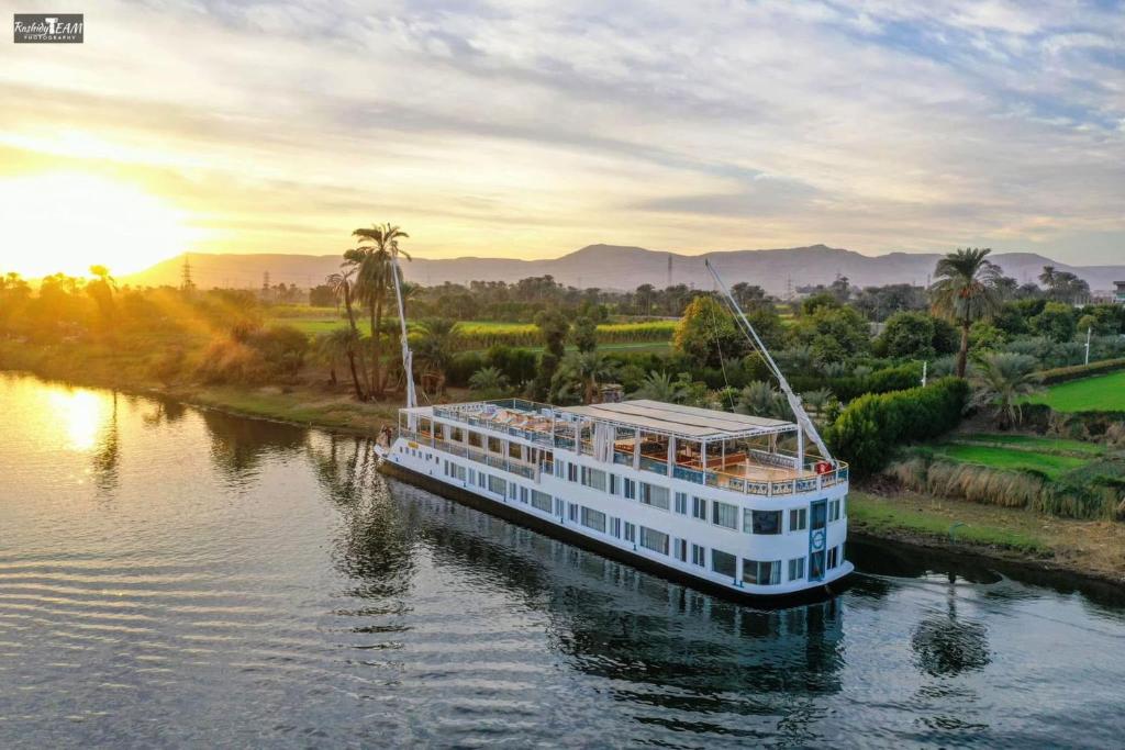 卢克索Embrace 2 Nile Sailing Dahabiya -Luxor- Aswan- 4 Nights的夕阳下的河上，一艘游轮缓缓驶过。