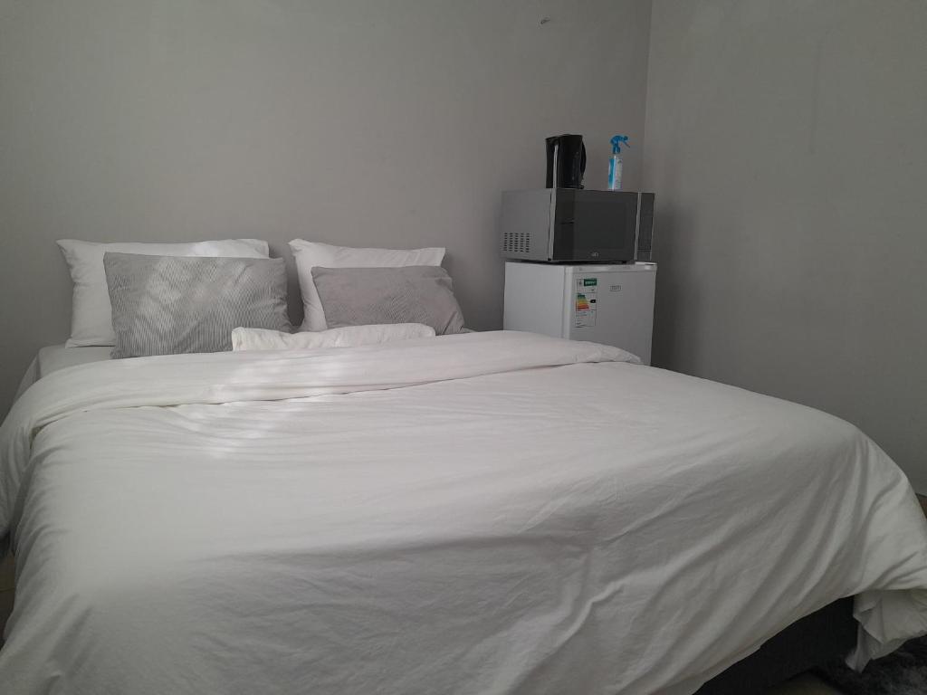 a white bed with white sheets and a refrigerator at Shalom Villa Guesthouse Walvis in Walvis Bay