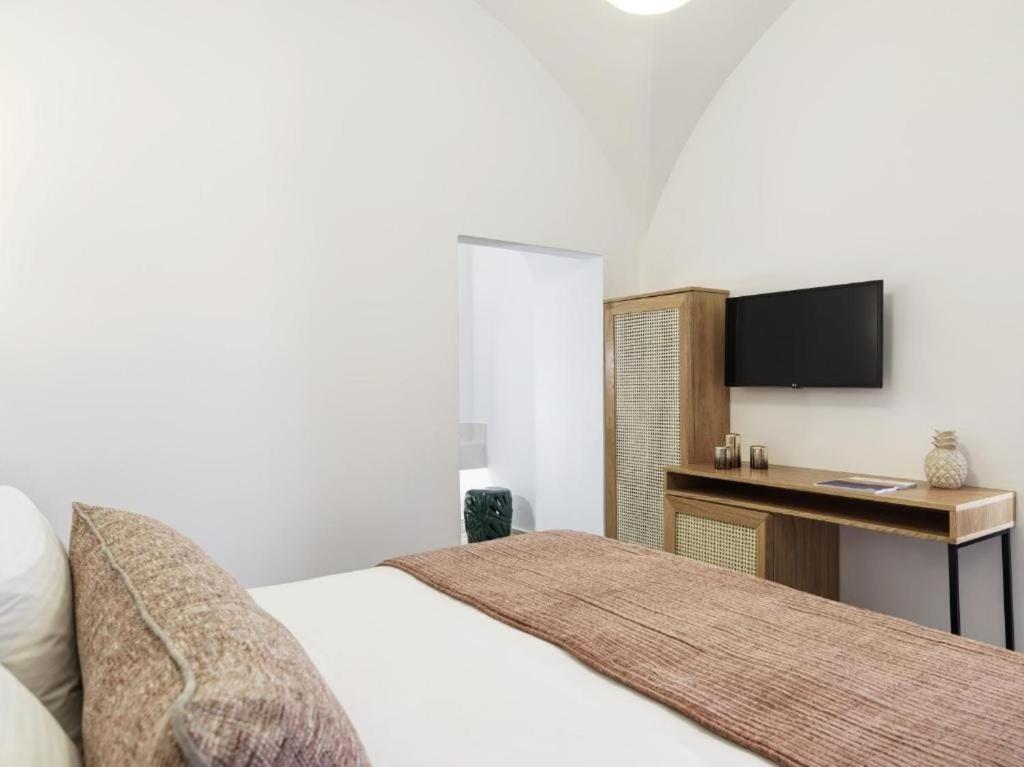 a bedroom with a bed and a desk with a television at Astris Suite, Mansion Double Room, Imerovigli in Imerovigli