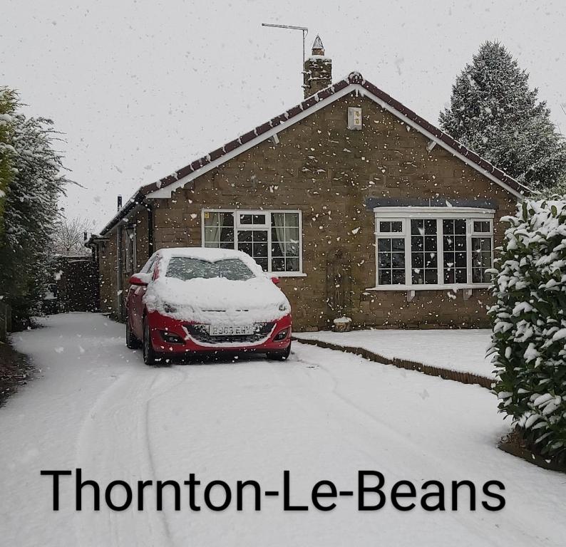 a red car parked in front of a house covered in snow at Willow Cottage 3 bed, cosy stopover, dogs welcome in Thornton-le-Beans