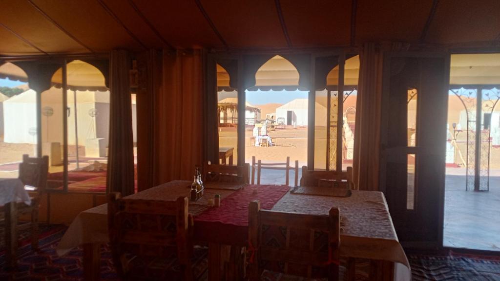 a dining room with tables and chairs and windows at Anssuf merzouga luxury camp in Merzouga