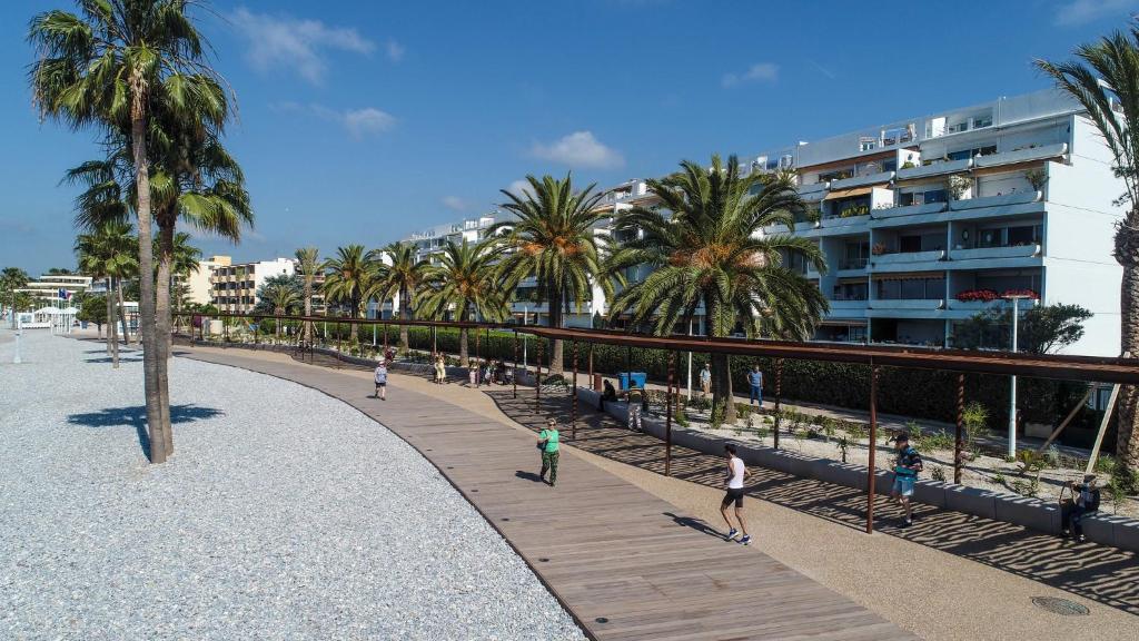 people walking on a boardwalk near a beach with palm trees at Appartement avec jardin - Front de mer St Laurent-du-Var in Saint-Laurent-du-Var