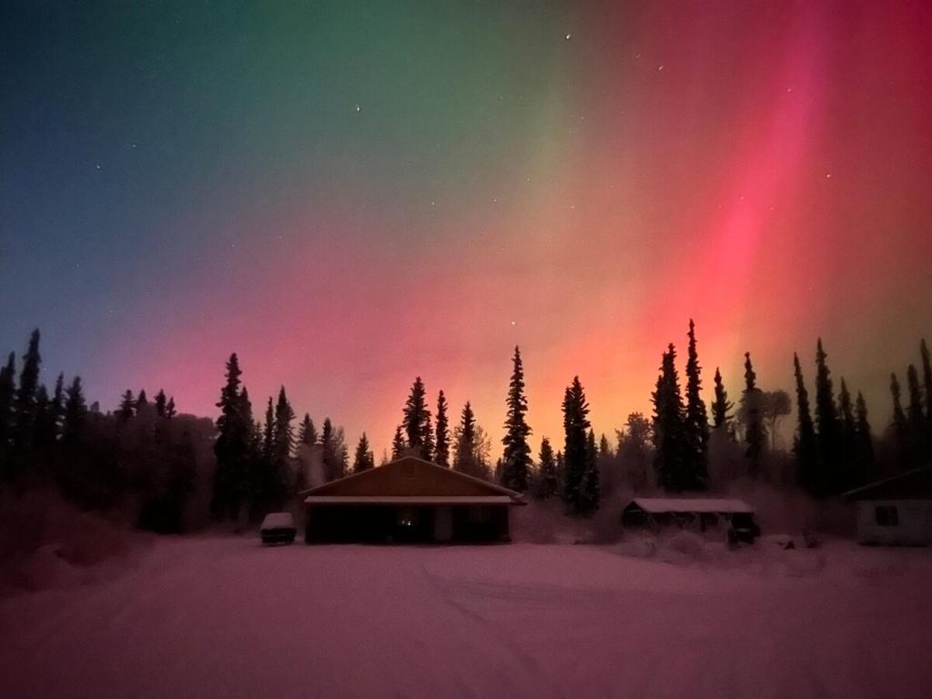 un'aurora nel cielo sopra una cabina con alberi di Northern Lights Getaway! a North Pole