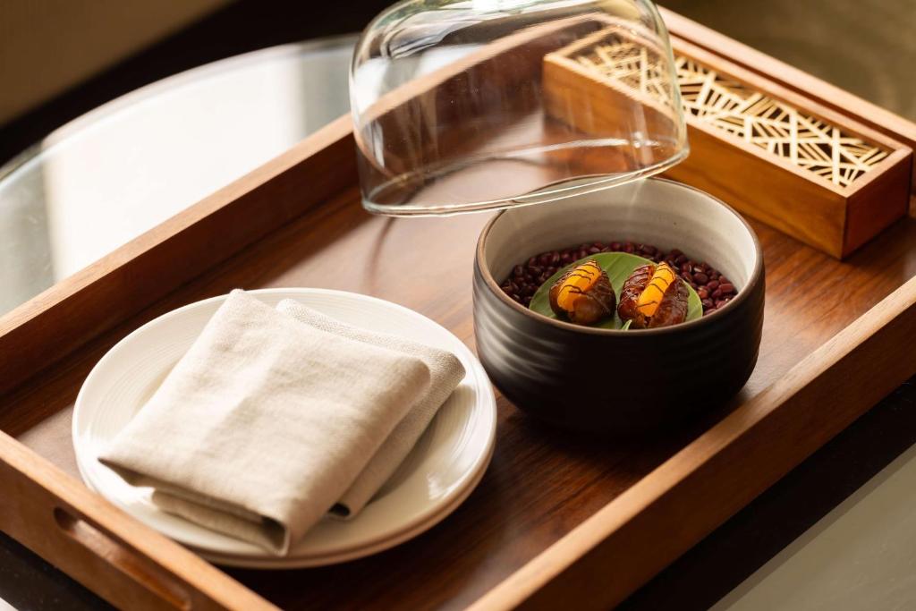 A covered tray presents a small bowl of fruit beside folded linen.