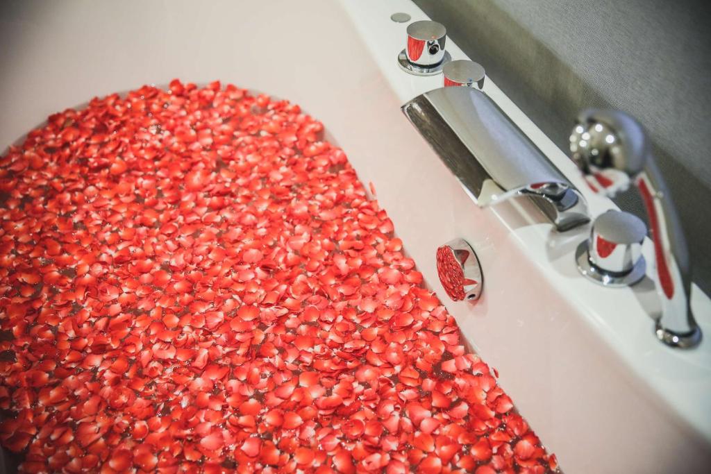 A white sink basin is filled with red flower petals beside chrome fittings.