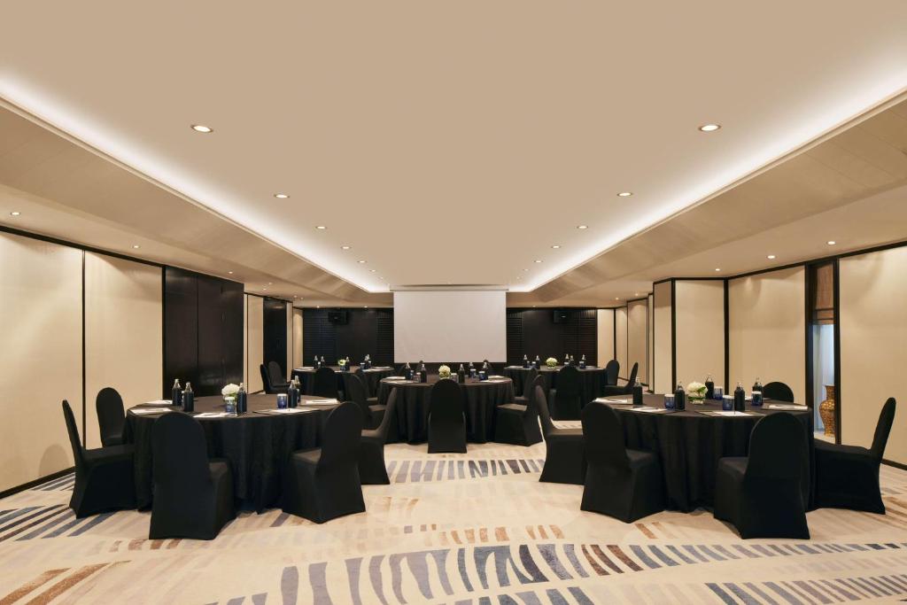 A spacious meeting room is set with round tables facing a central projection screen.