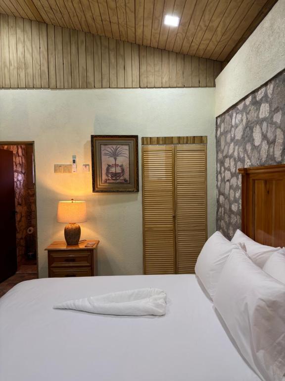 ein Schlafzimmer mit einem weißen Bett und einem Nachttisch mit einer Lampe in der Unterkunft The Ridge - Stone Cottage in Buff Bay