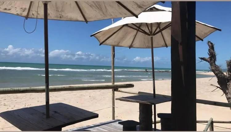 two tables and umbrellas on a beach with the ocean at Pousada Ventoria in Canguaretama