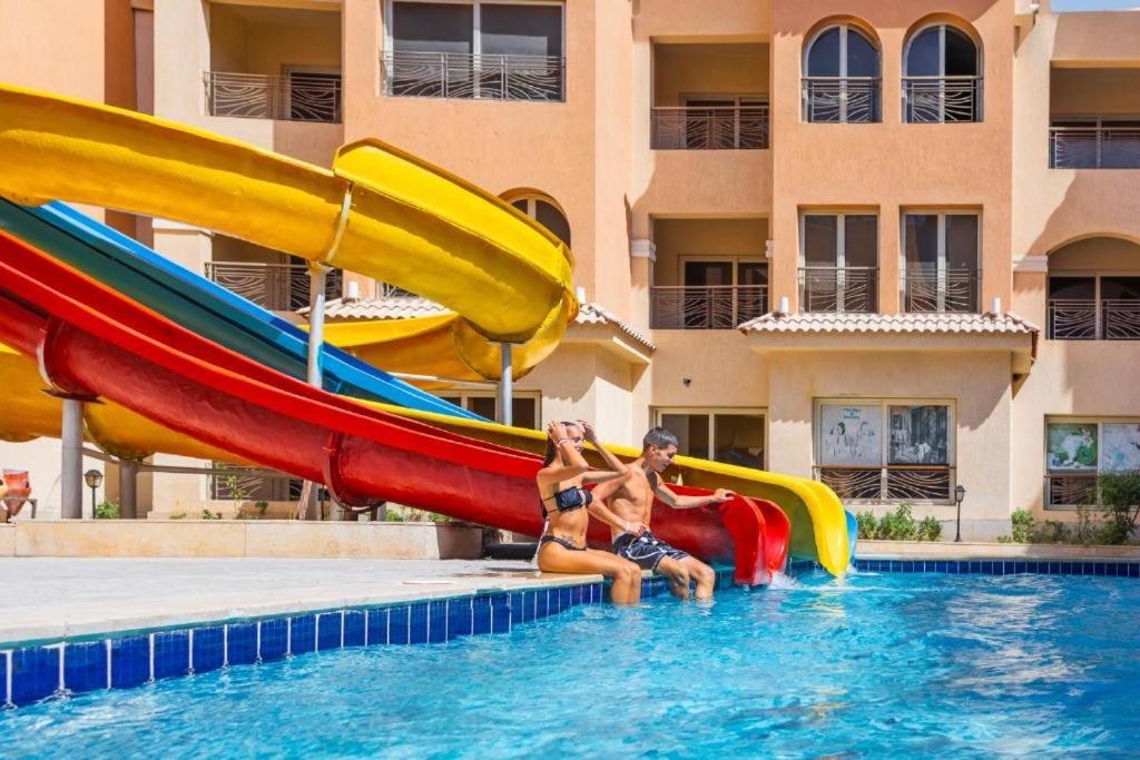 a man and a woman sitting on a slide in a pool at Rosa Boho Hotel And Aqua Park in Hurghada