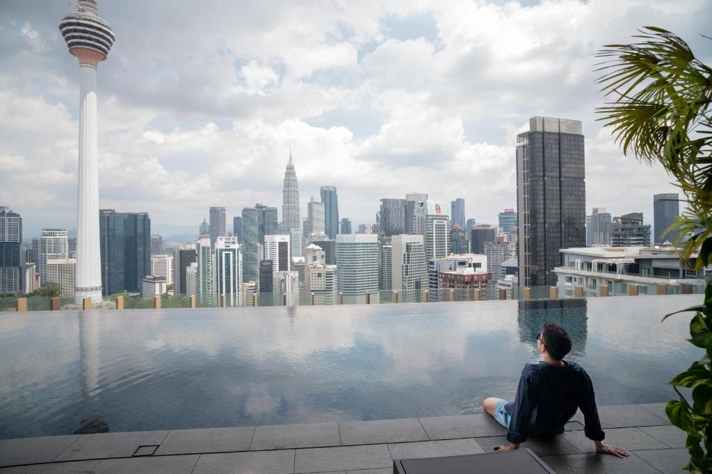 a woman sitting on the edge of a pool overlooking a city at Ceylonz Suites KLCC Rooftop Infinity Pool KL Tower View in Kuala Lumpur