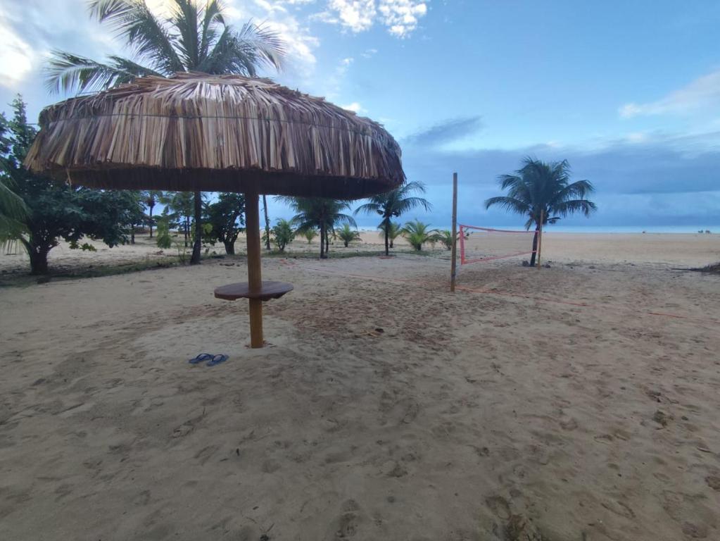 a straw umbrella on a beach with palm trees at Apartamento à beira-mar em São Miguel do Gostoso in São Miguel do Gostoso