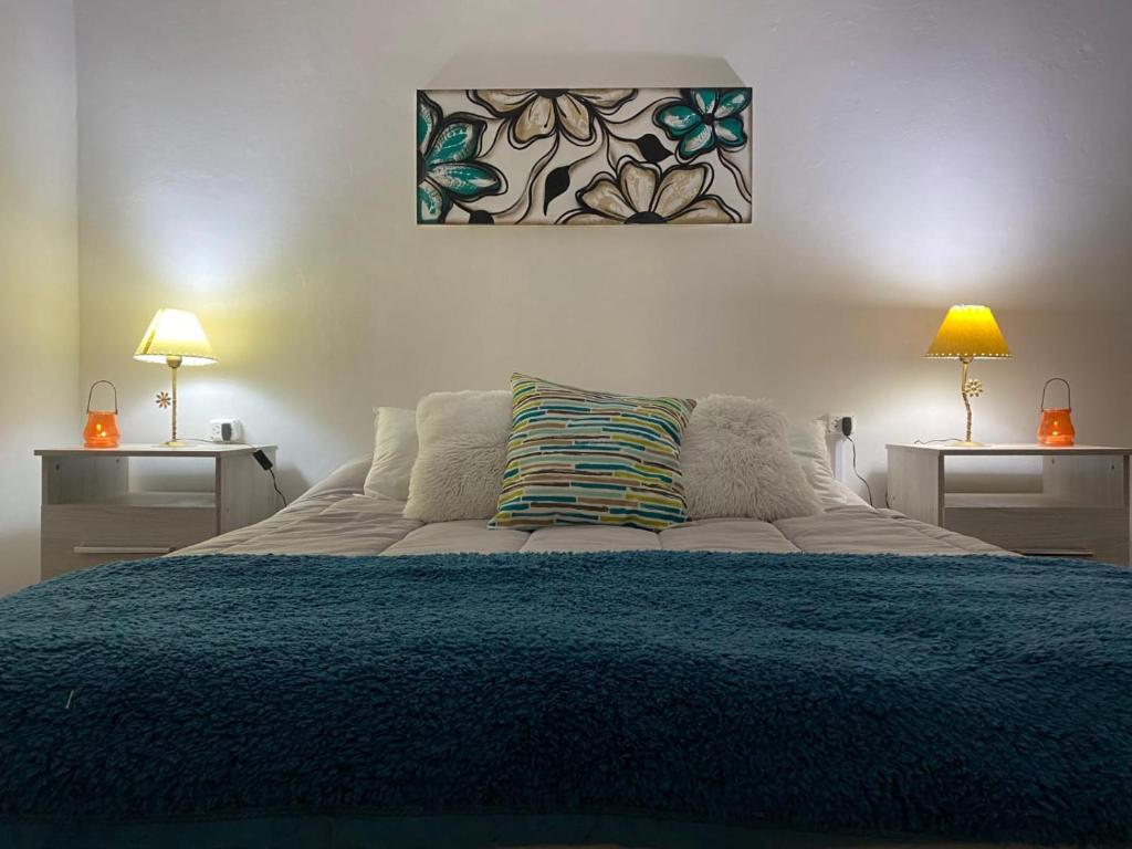 a bedroom with a bed with a blue blanket and two lamps at Sol de Mayo in Tinogasta