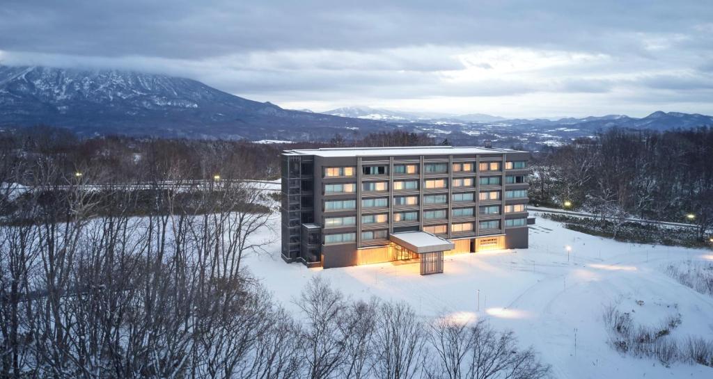 a building in the snow with mountains in the background at Hinode Hills Niseko Village in Niseko