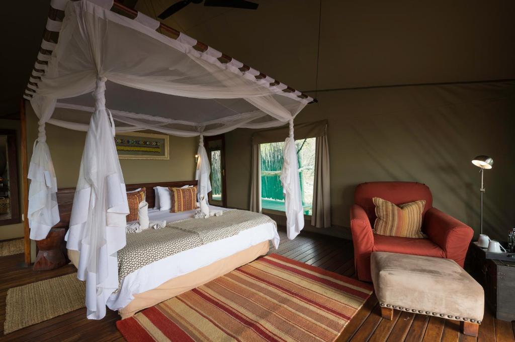 a bedroom with a canopy bed and a red chair at Ongava Tented Camp in Okaukuejo