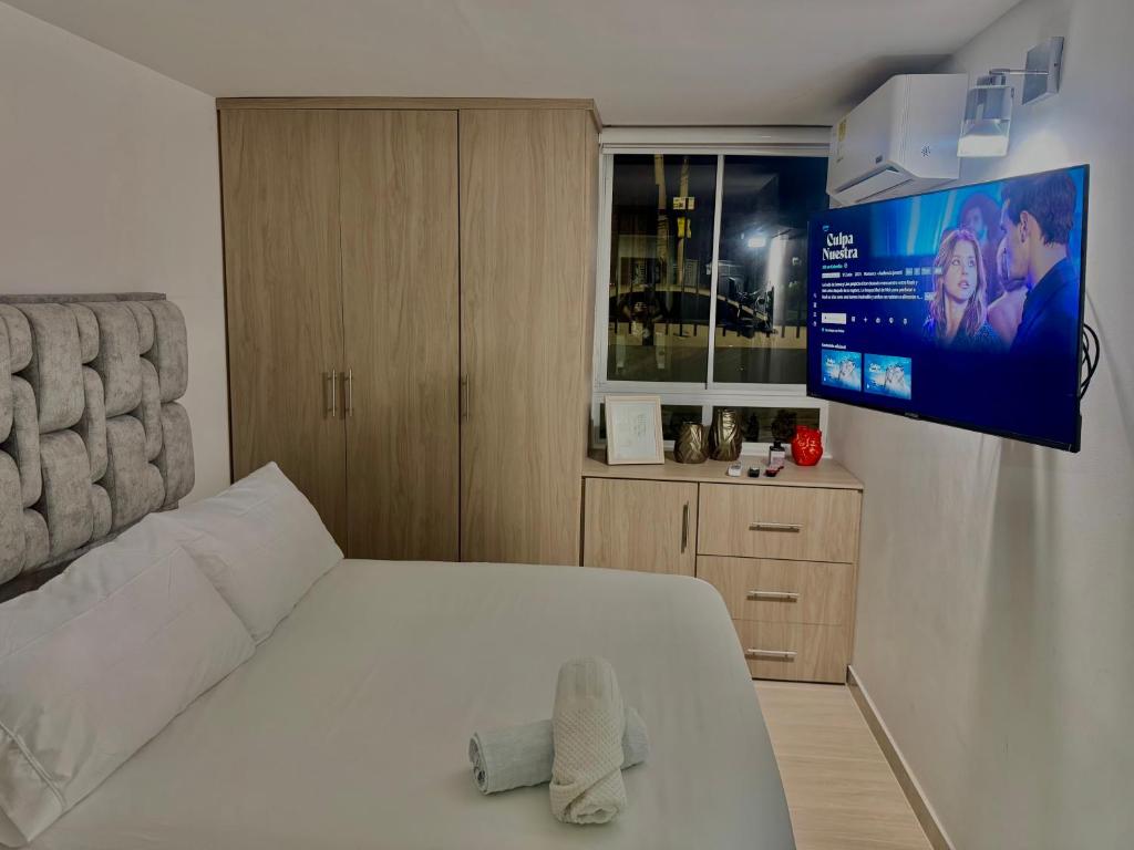 Acogedor Apartamento al oriente de Neiva في نيفا: غرفة نوم بسرير ابيض وتلفزيون على الحائط
