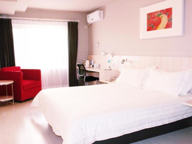 a bedroom with a white bed and a red chair at Jinjiang Inn Changchun City Hall in Changchun