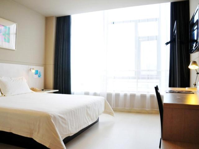 a bedroom with a bed and a desk and a window at Jinjiang Inn Wujiang Zhongshan North Road in Suzhou