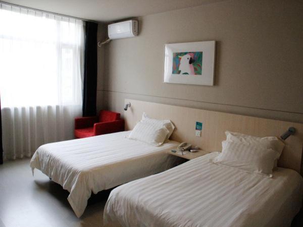 Cette chambre d'hôtel comprend deux lits et un fauteuil rouge. dans l'établissement Jinjiang Inn Chengdu Dufu Thatched Cottage, à Chengdu