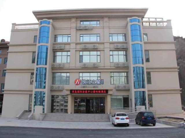 een groot gebouw met auto's geparkeerd voor het bij Jinjiang Inn Select Qingdao International Exibition Centre Miaoling Road in Qingdao