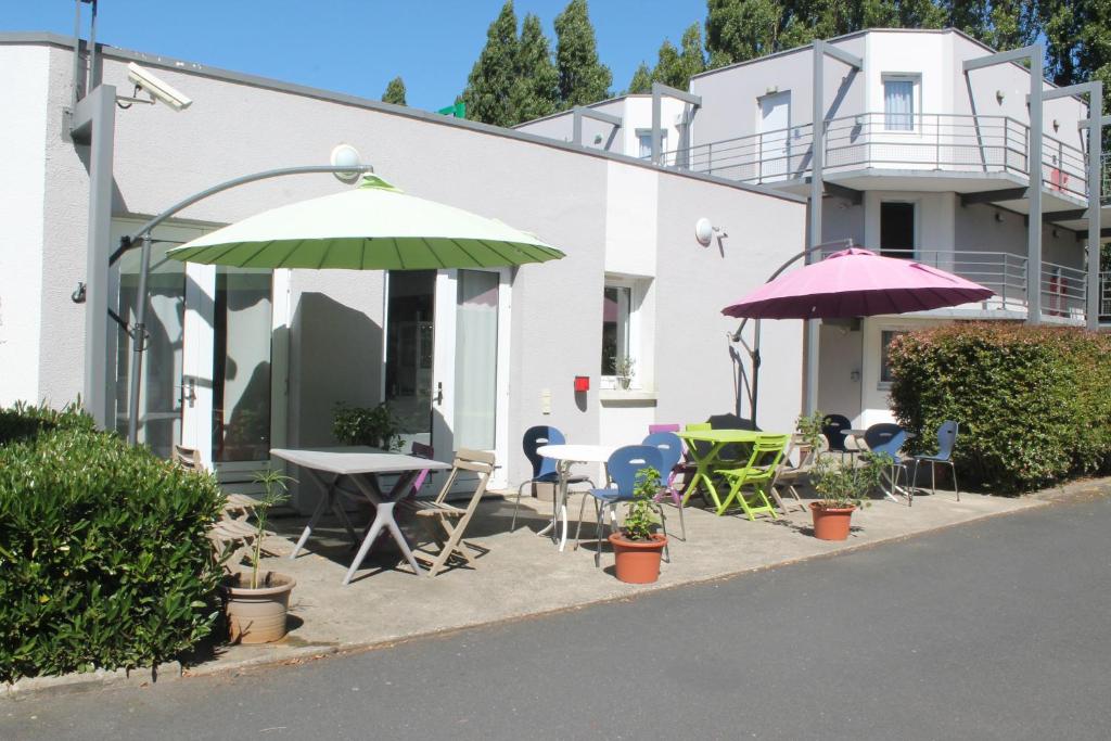 un patio con sillas, mesas y sombrillas frente a un edificio en B Hotel Caen Mondeville, en Mondeville