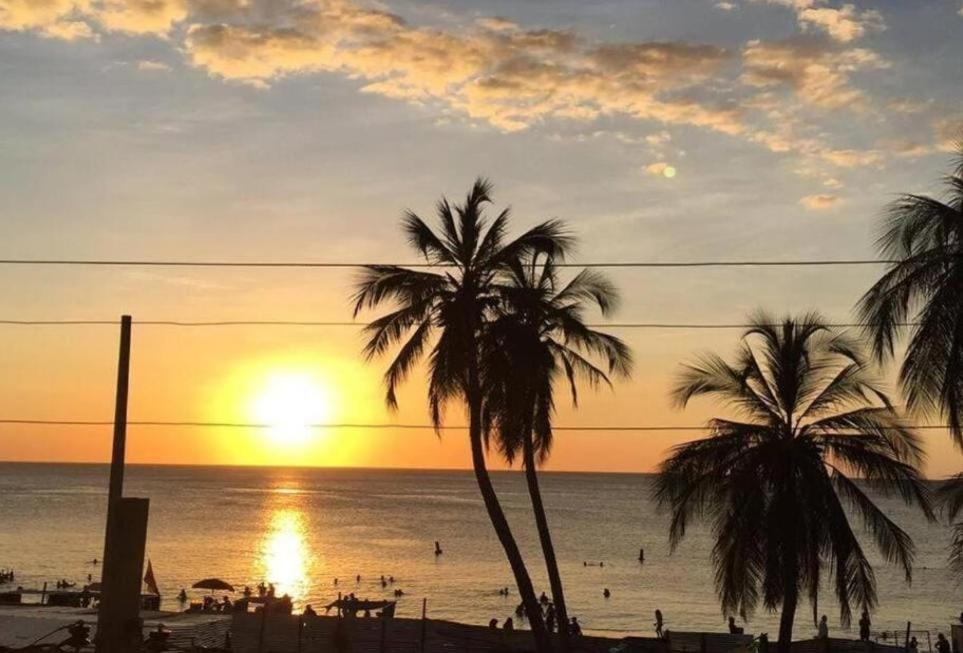 a sunset on a beach with palm trees and the ocean at Apartamento frente al mar y la playa Rodadero in Rodadero