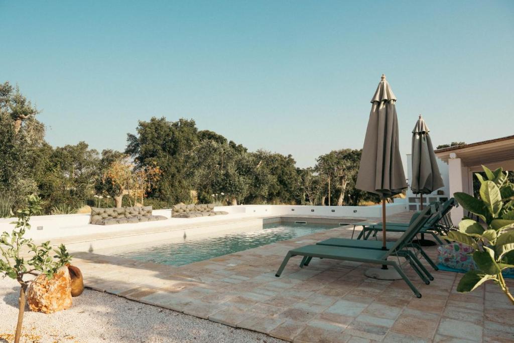 une piscine avec deux chaises et un parasol dans l'établissement Villa Jolie con piscina, à San Vito dei Normanni
