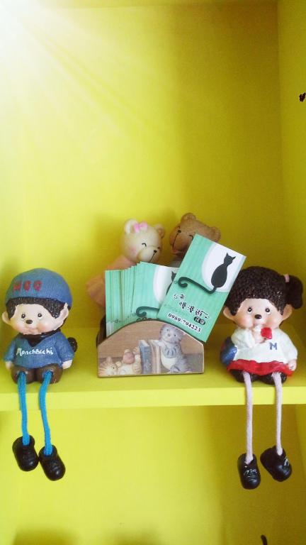 a shelf with dolls and books on a yellow wall at Slowly B&amp;B in Taitung City