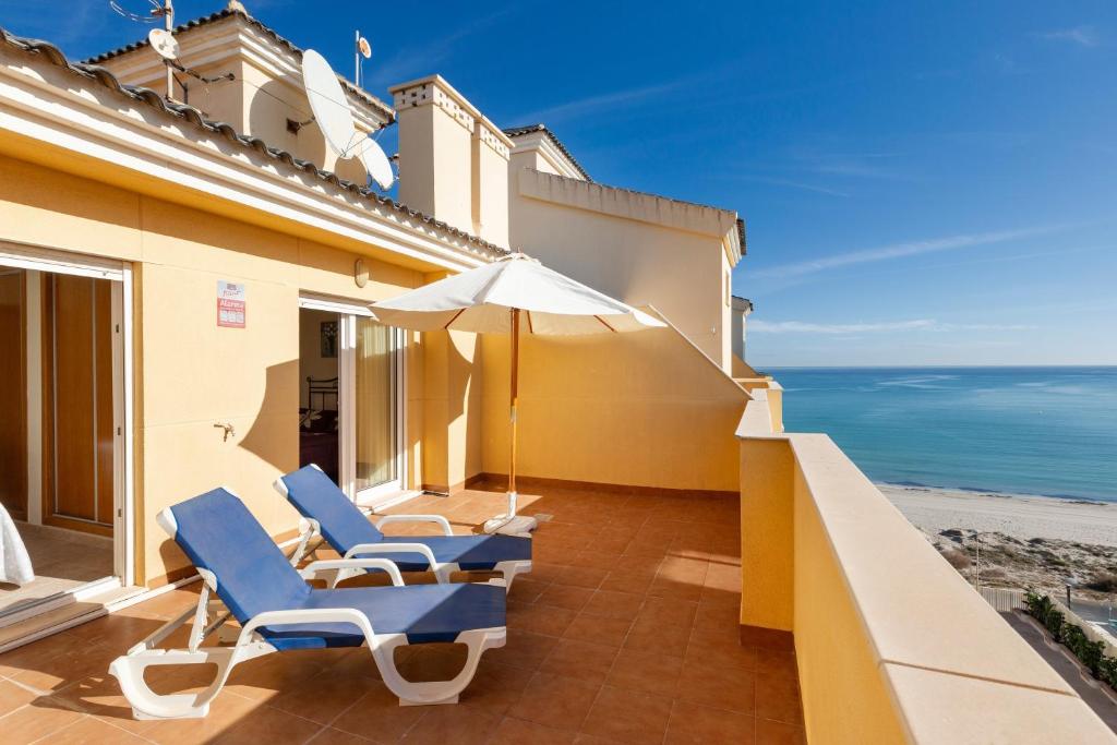 a balcony with chairs and an umbrella and the ocean at Beachfront penthouse in La Manga in San Blas