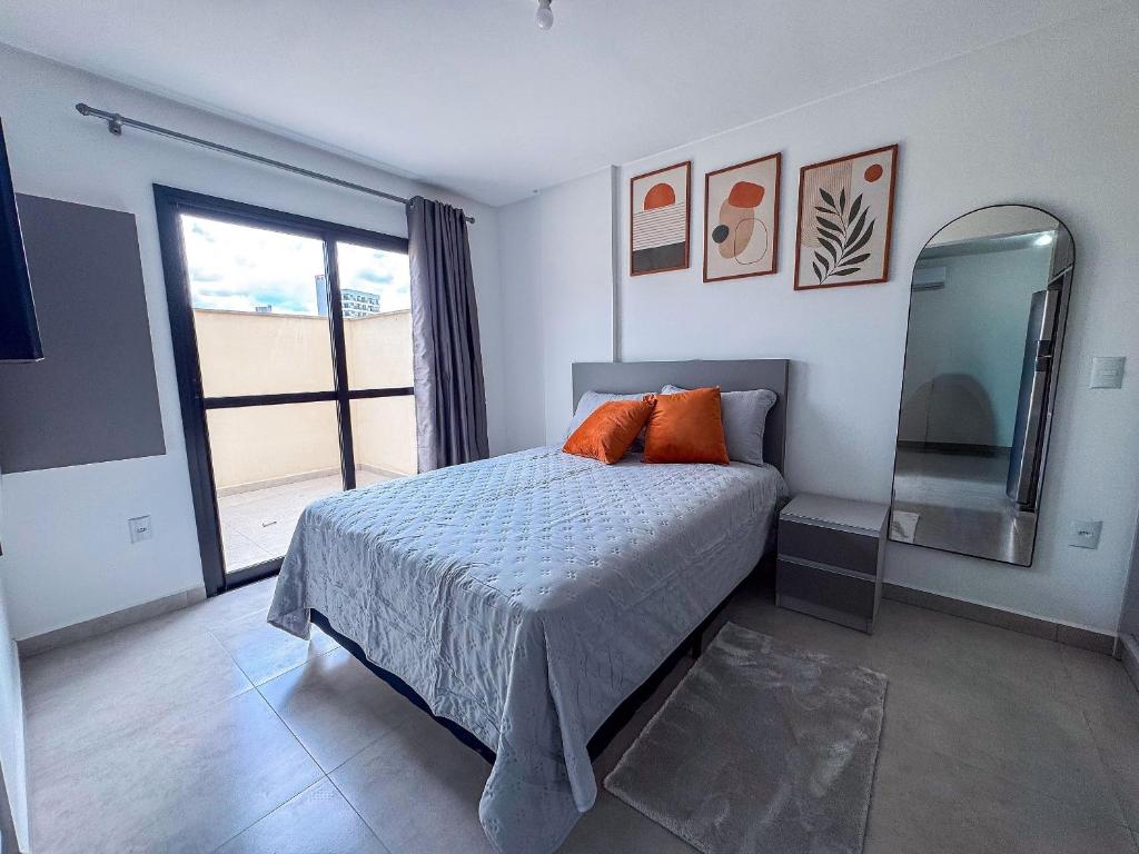 ein Schlafzimmer mit einem Bett mit orangefarbenen Kissen und einem Spiegel in der Unterkunft Studio Novo e Completo Próx. Faculdade e Shoppings in Limeiro