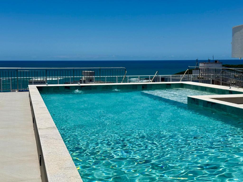 a swimming pool with the ocean in the background at Peracanga Bacutia Guarapari Ls06 in Guarapari