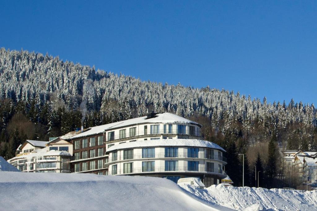 a building covered in snow in front of a mountain at Czarna Perła Apartamenty z bezpłatnym basenem Czarna Góra Resort in Sienna