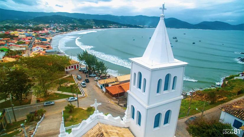 a white church with a steeple next to a beach at Apartamento de 2 Quartos para 4 Pessoas - 5 min da Praia in Garopaba
