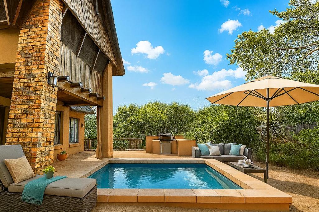 a swimming pool with an umbrella next to a house at Adventure Bush House II in Marloth Park