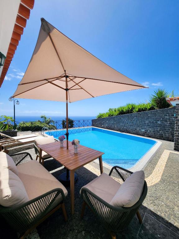 ein Tisch mit Sonnenschirm neben einem Swimmingpool in der Unterkunft Villa Ocean Wave Calheta - Oversized Pool & Stunning Ocean Views in Calheta