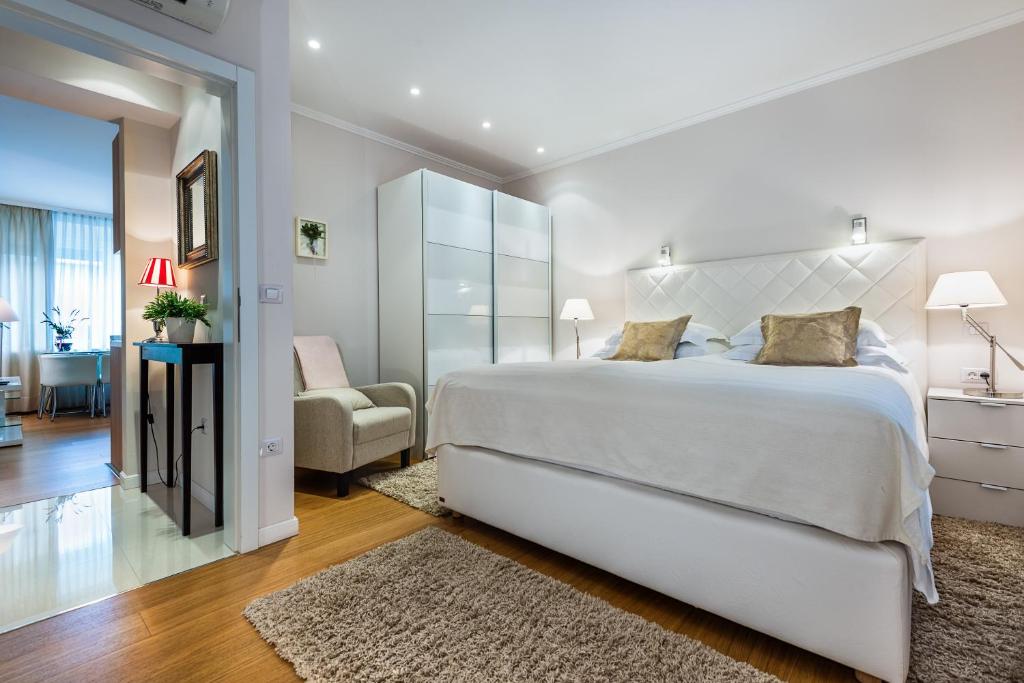 a white bedroom with a large bed and a chair at Madison Luxury Apartments & Rooms in Zagreb
