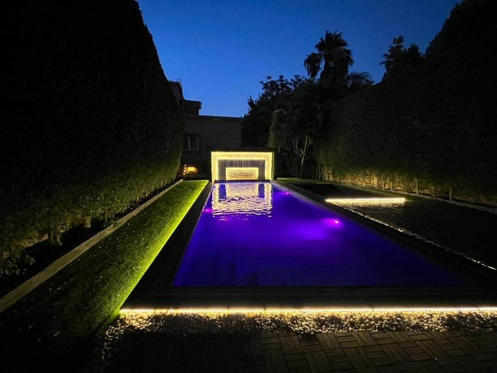 une piscine avec des lumières dans un jardin la nuit dans l'établissement Velora 4 BR Villa With pool and waterfall in New Cairo, au Caire