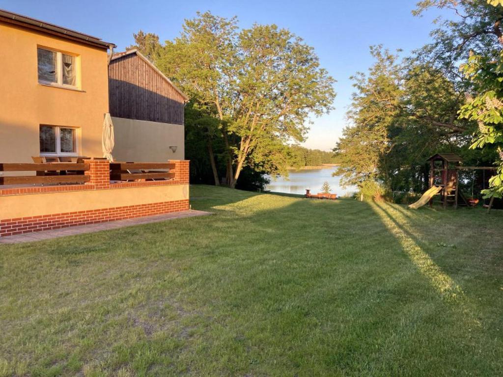 a house with a grassy yard next to a lake at Ferienwohnungen Zur Biberburg in Friedrichswalde