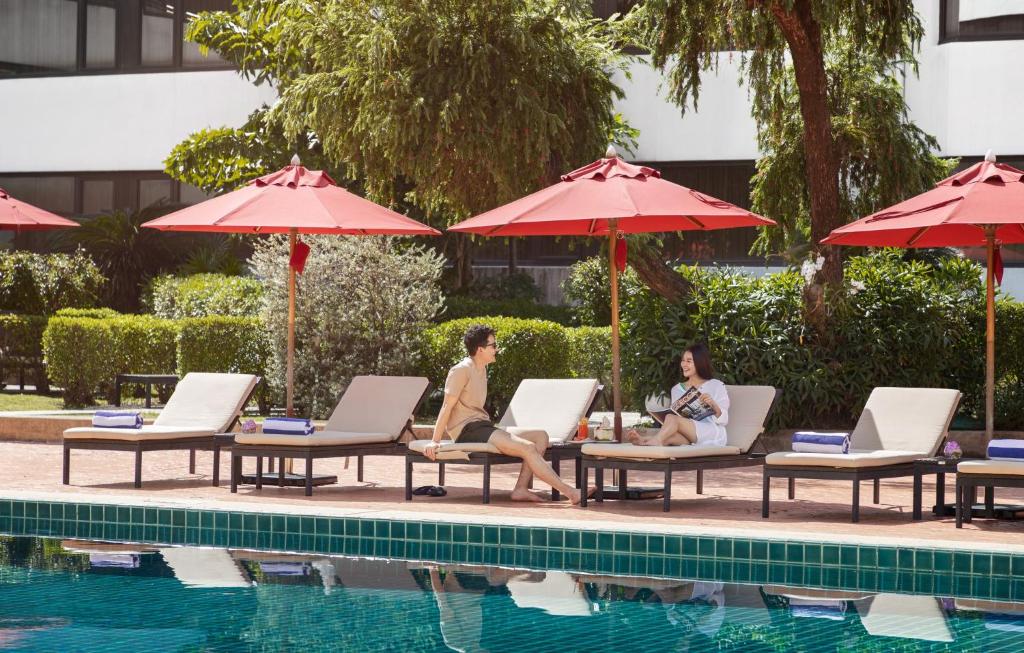 A landscaped outdoor pool is lined with loungers and red parasols.