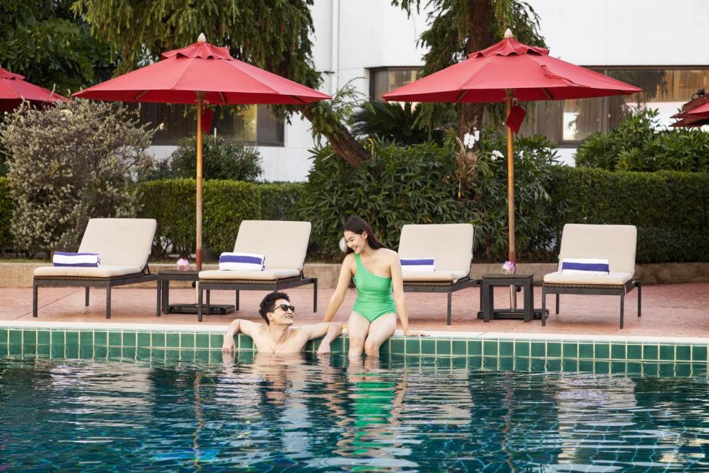 A poolside scene with swimmers, loungers and red umbrellas.