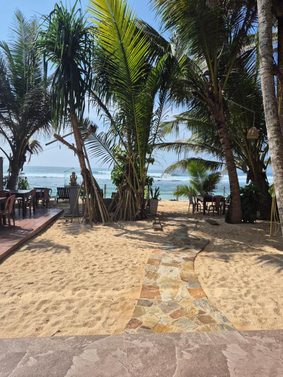 einen Strand mit Tischen, Palmen und dem Meer in der Unterkunft Blue Corals Beach Bungalow in Madihe East