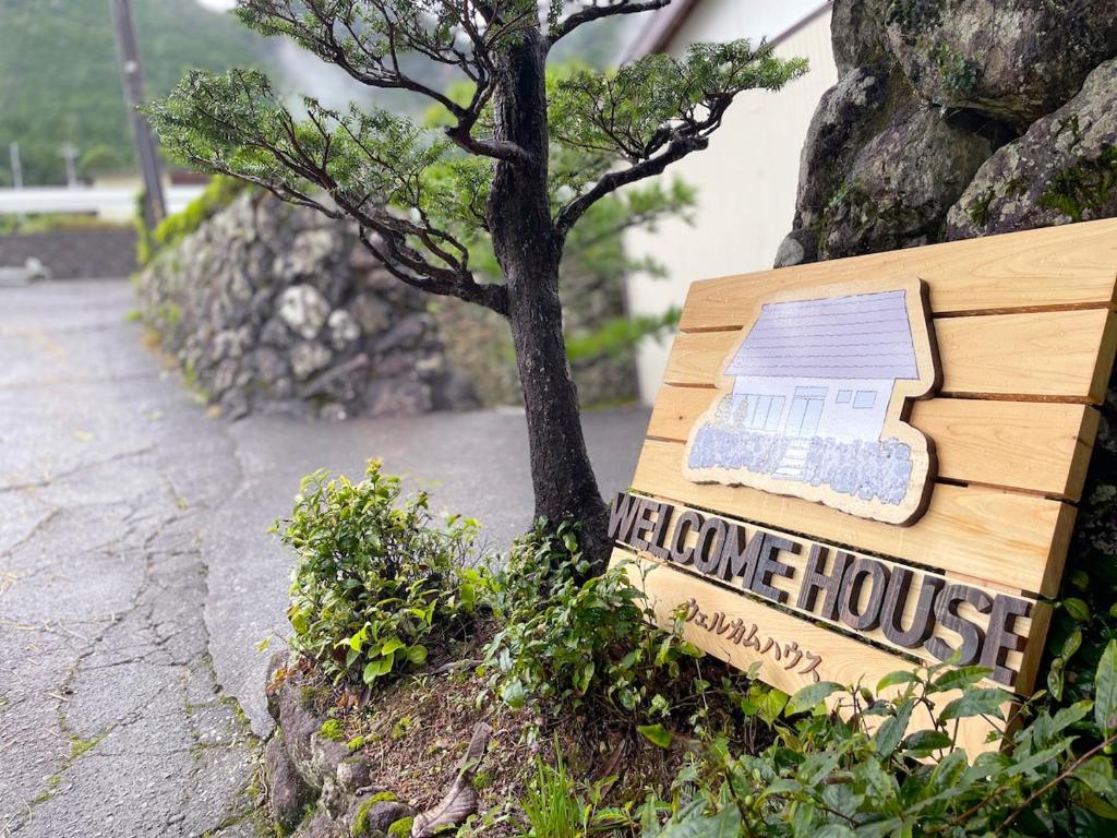 Ein Schild mit der Aufschrift „Wir kommen nach Hause“ steht neben einem Baum. in der Unterkunft 星空と田園風景のウェルカムハウス in Uwano