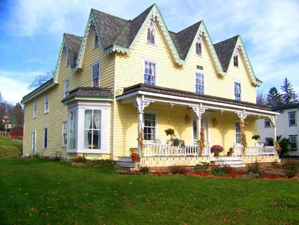 ein gelbes Haus mit einer Veranda und einem großen Garten in der Unterkunft Stamford Gables Bed and Breakfast in Stamford