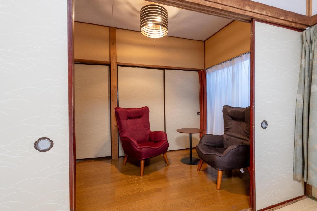a room with two red chairs and a table at ぱんだホステル三ノ輪 Panda Hostel Minowa in Wada