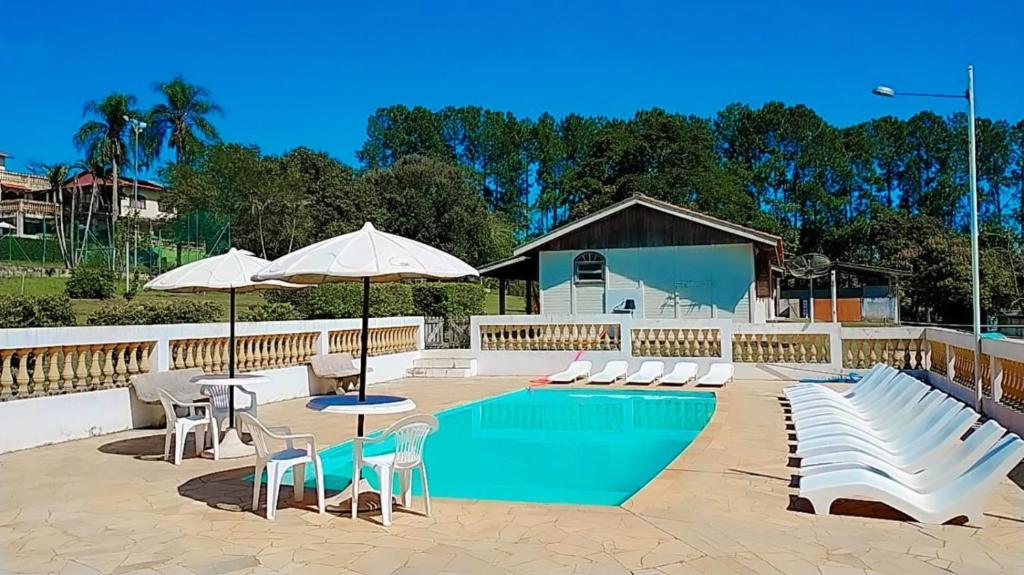 a pool with white chairs and tables and umbrellas at Estância Flor do Campo in Sarapuí